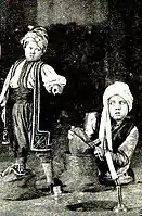 Still for the American film Ali Baba and the Forty Thieves with Ali Baba (George Stone) being asked by his rich brother the secret of the cave, from pages 16 and 17 of the February 1919 Film Fun