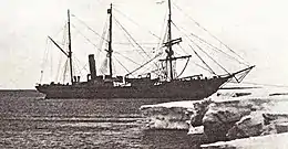 Three-masted ship with funnel to rear, anchored by the bow to an ice shelf