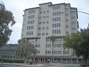 a ten-story building with sable palms, a Spanish moss-drapped oak tree, hedges, and a court yard