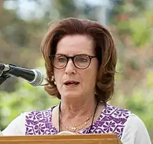 Brown-haired woman wearing glasses at podium with microphone