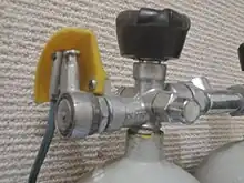 Close up of a Draeger reserve valve, showing the plastic guard and the connection of the operating lever, which is held on by a spring loaded pin and which can be adjusted to several angles. depending on which of the holes on the reserve spindle the pin engages.