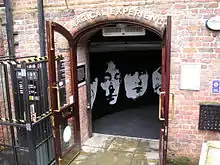 Arched doorway through a weathered red brick wall with sign "Magical Experience" above. On the wall inside the doorway is stylised silhouette of the four Beatles members