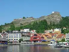 Modest buildings along the water's edge are guarded by a fortress on the hill above.