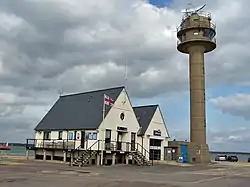 white double building with dark grey roofs beside a tall brown tower