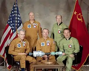the five crew members of ASTP sitting around a miniature model of their spacecraft