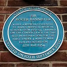 Blue circular plaque which reads: City of Westminster – unveiled on 10th September 2000 – Sir Roger Bannister – while a medical student at St. Mary's hospital medical school from 1951–54, trained on the cinder track on this site in preparation for the first under 4 minute mile run in Oxford on 6th May 1954.