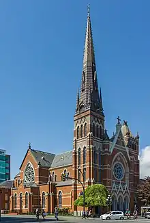 Exterior view of a red brick cathdral with a large spire built into a corner