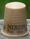 An off-white thimble, with the visible black lettering, "NIXON/Put the ne ...