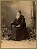 Turkish woman, full-length portrait, seated, facing front, holding parasol.