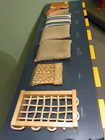 Touchable museum samples illustrating a 1590s bed: the bedcords, plaited-rush bedmat, a flockbed and a featherbed in dun ticking, a downbed in striped ticking, and the bedlinen.