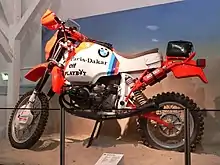 Race-prepared R 80 G/S motorcycle, with Paris Dakar, Elf, and Playboy stickers. Displayed on a stand in a museum